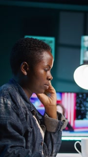 Vertical video African american woman working from home, using laptop, looking at statistic charts. Remote worker in personal apartment