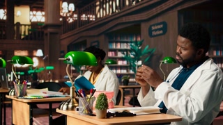 Medical student practices dentistry techniques with a plastic jaw model in a library, doing physical research for stomatology thesis