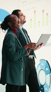 Vertical video Corporate managers evaluate fiscal performance metrics on digital wall, collaborating. Diverse executive team discusses