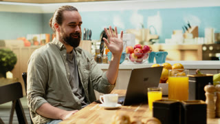 Professional man attending video online meeting on laptop, greeting colleagues on conference and waving hand. Adult briefing and sharing