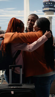 Vertical Video Emotional scene of African American parents hugging daughter in airport terminal, saying a bittersweet goodbye before