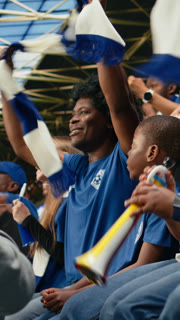 Vertical Video Black family celebrating with young child during exciting soccer match in packed stadium, cheering for blue team. Parents