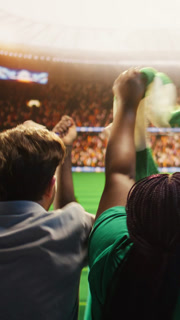 Vertical video Rear view of happy fans celebrating goal from stadium stands during football match. Back view of jolly soccer supporters