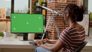 African american freelancer working from home with greenscreen on computer, at desk. Using chroma key template with isolated mockup display and blank copyspace background. Tripod shot.