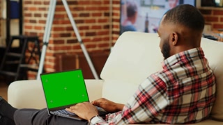 Focused remote freelancer working from home, typing data on chroma key mock up laptop green screen. African american teleworker solving