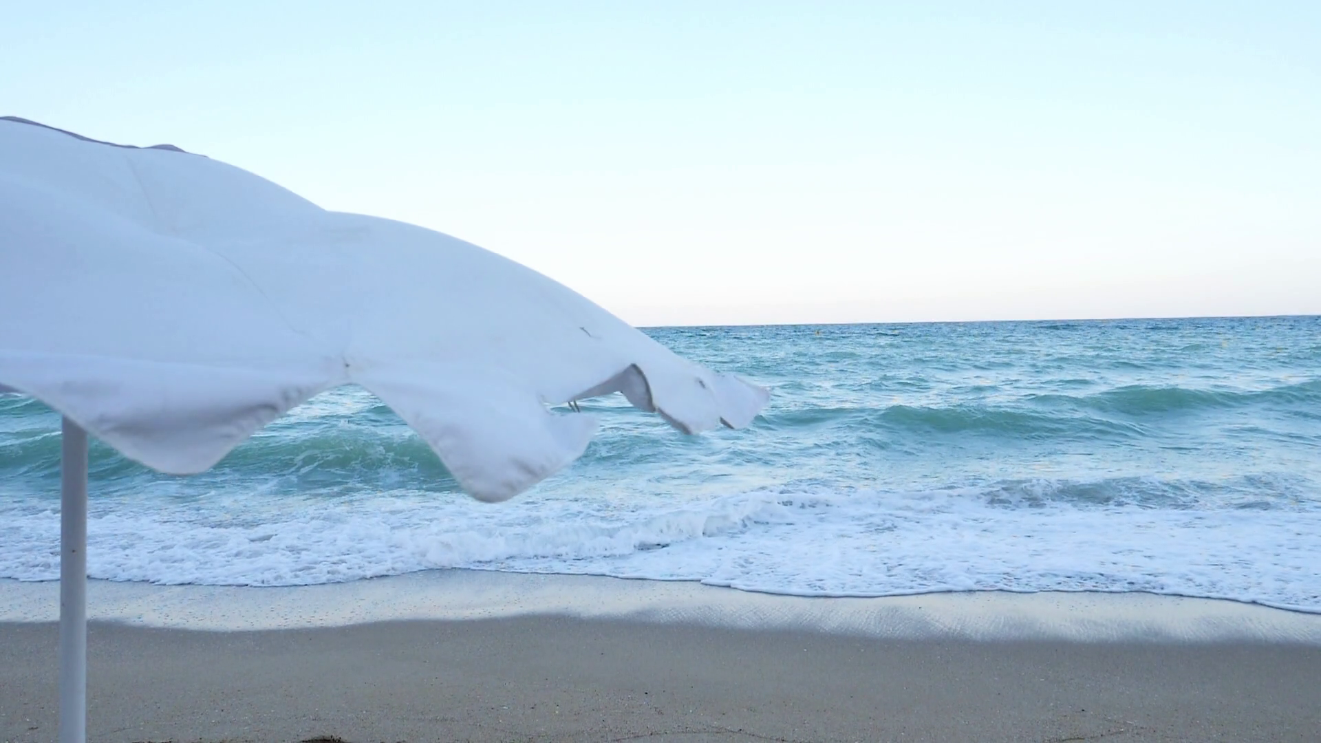 Beach umbrella blowing in the wind near the sea. Slow motion footage