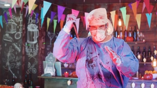Halloween costume of a mad psycho doctor with a bloody knife in his hand. Crazy medic killer costume dressed by an adult man in a decorated bar.