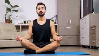 Man at home practicing yoga in the living room. He sitts in the lotus pose meditates. Dolly slider 4K footage