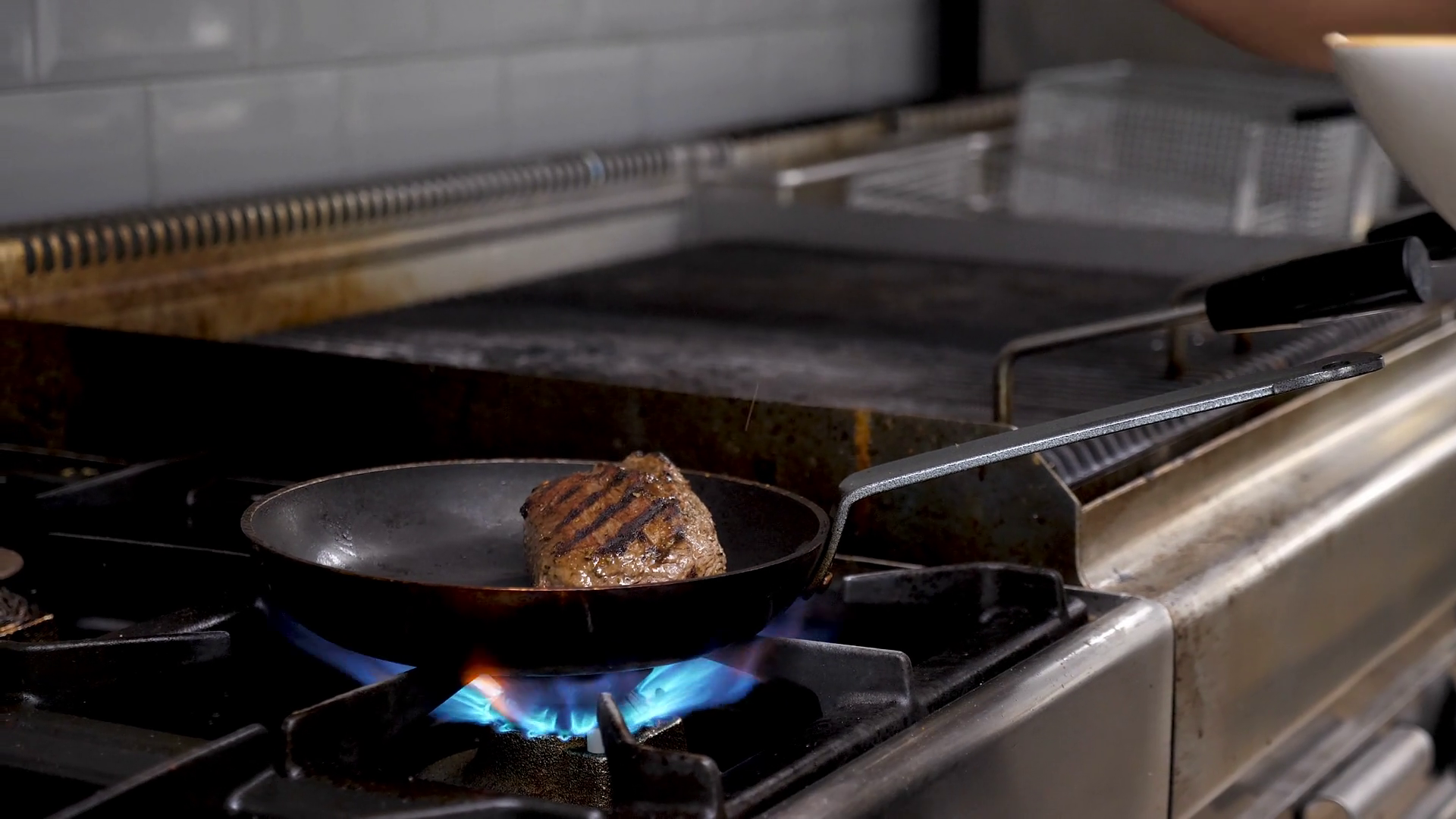 Pouring souce on piece of grilled fryed beef meat in restaurant kitchen