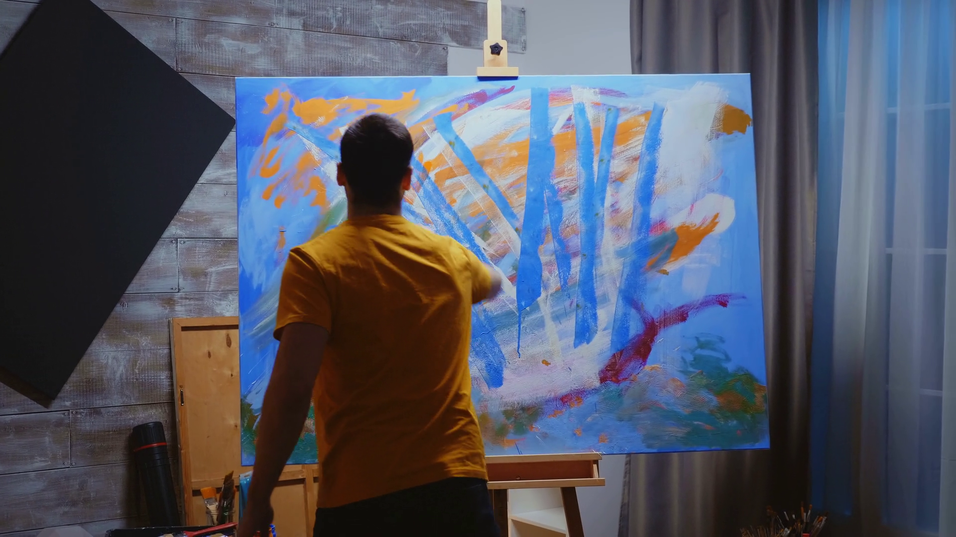 Young artist painting on canvas with roller as paint brush in art