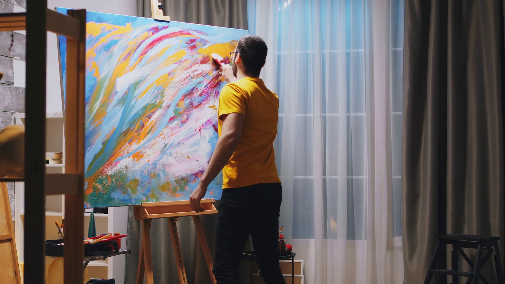 Young man painting on large canvas in art studio for exhibition on