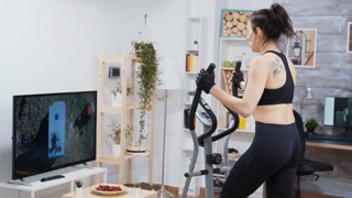Woman exercising while watching TV on elliptical machine.