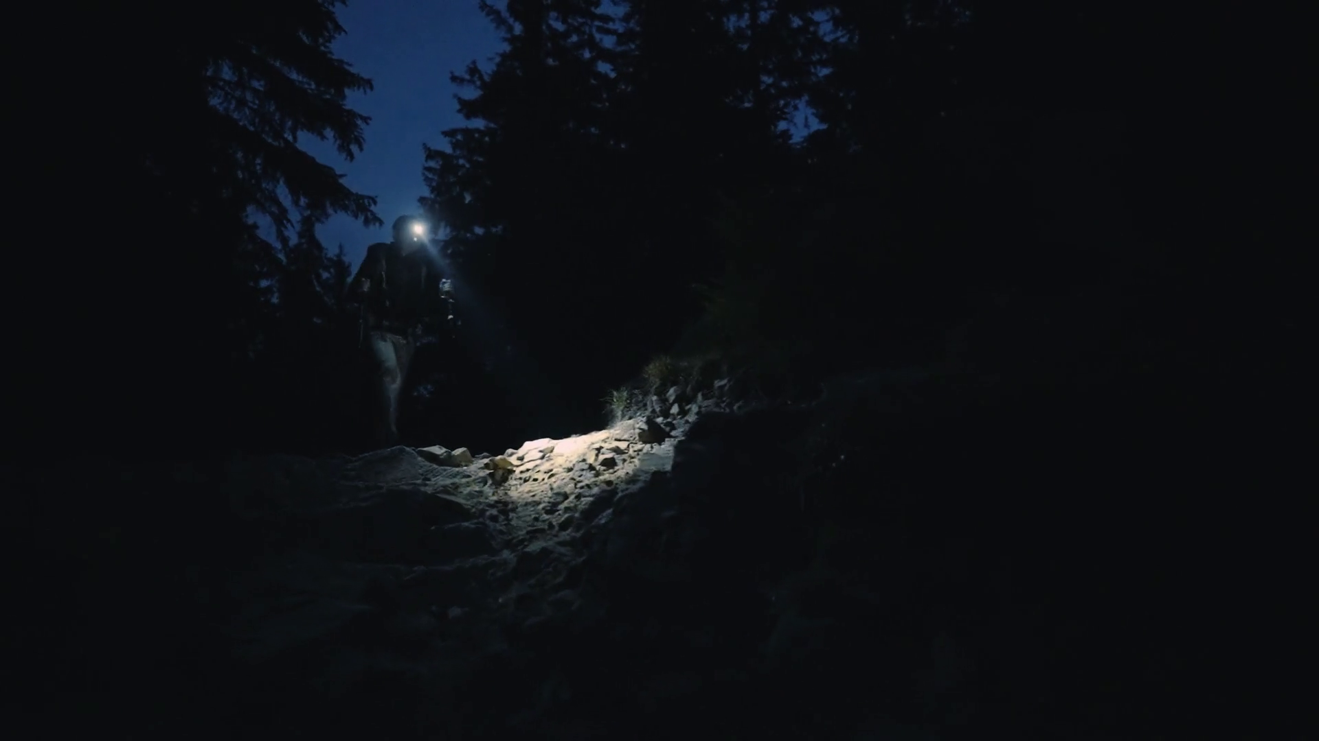 Man walk hiking through a dark rocky mountains shining through