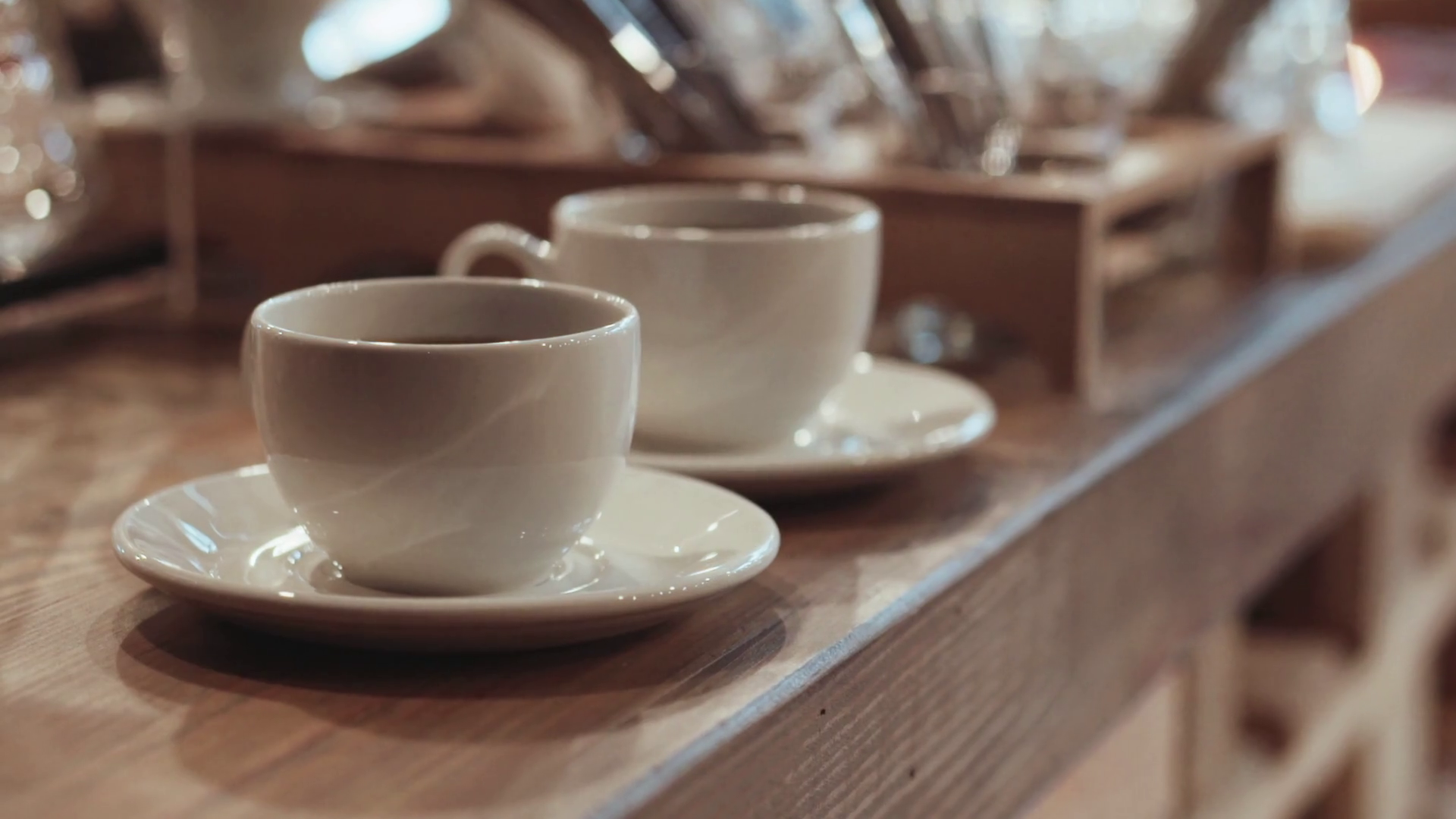 Two glittering white cups with coffee on a soft oak counter waiting for