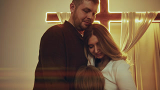Christian family praying together in church before a luminous cross