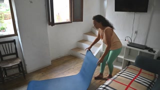 Woman setting up a yoga mat at home in a bright, cozy living room ready for exercise and relaxation sessions