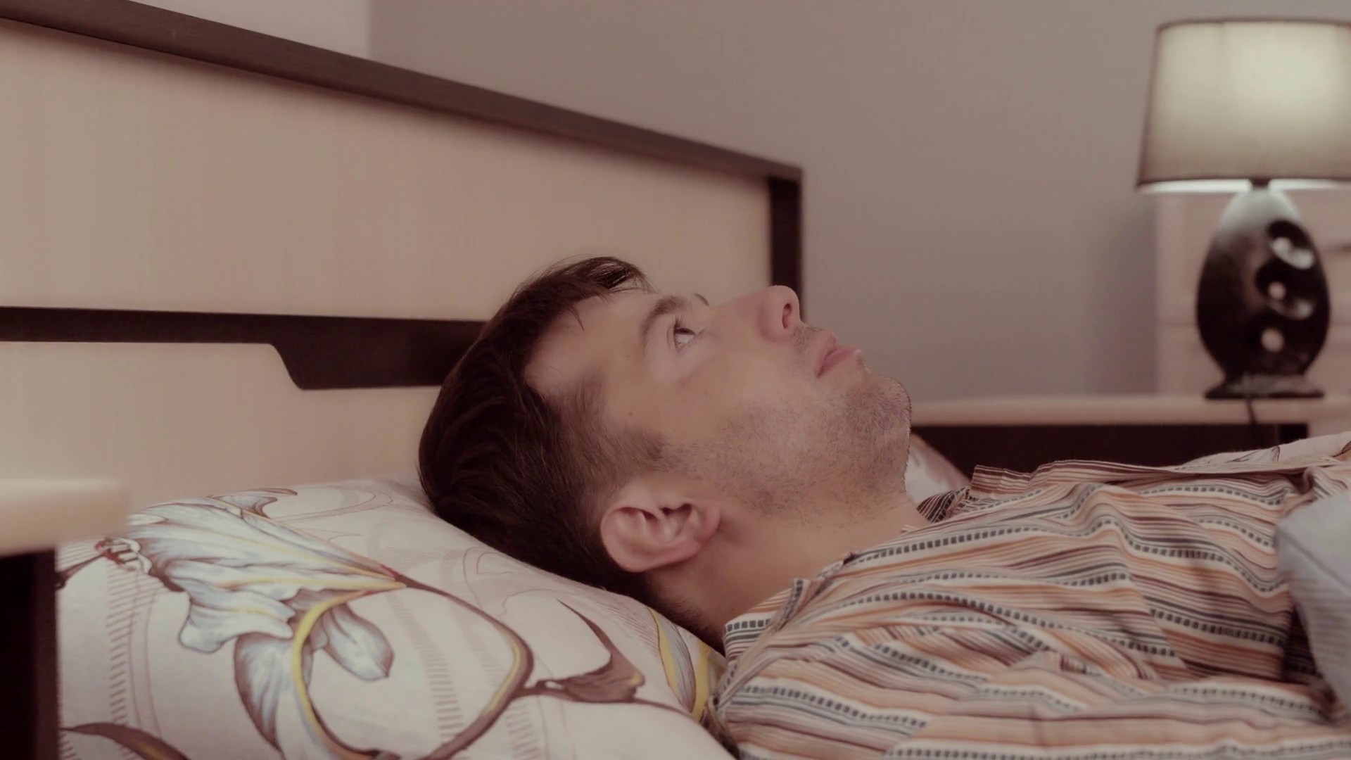 Young man lies frightened in bed and covers his head with blanket and