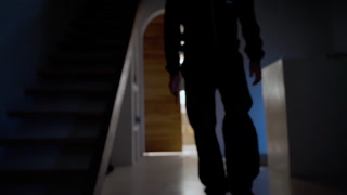 Hooded man holding a knife walking in a dark hallway