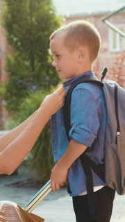 Caring mother helps her little school son and correct collar on shirt of son stroking child on head talking to schoolboy pupil near school