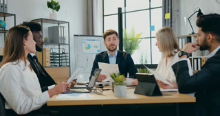 Business concept where good-looking positive confident bearded boss talking to his multiracial male and female corporate coworkers during briefing in office room