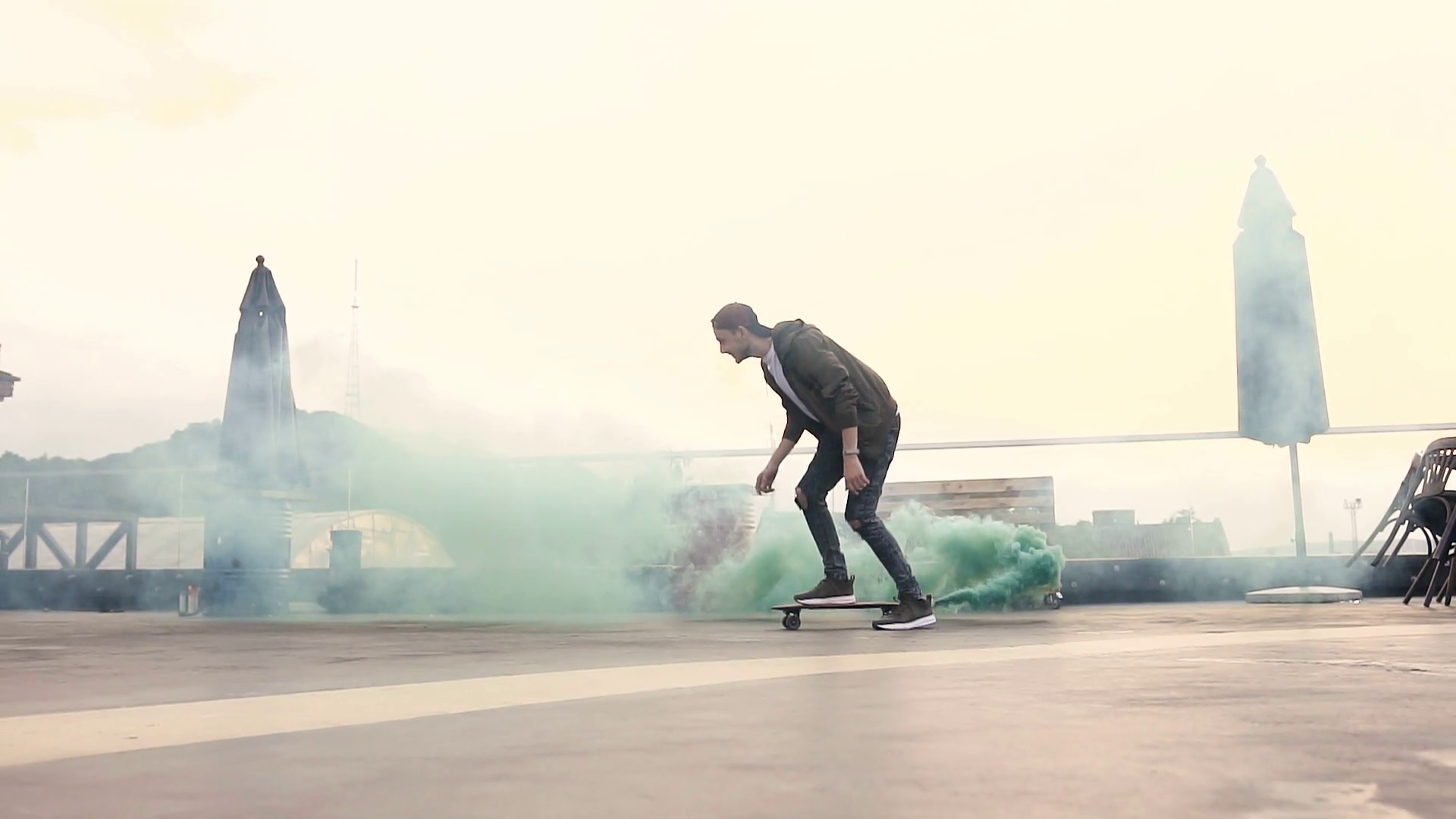 Handsome hipster guy skateboarding rides with colored smoke on the