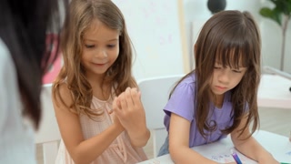 Teacher guiding child in coloring book at school. Multi-cultural classroom with preschoolers. Education and learning.