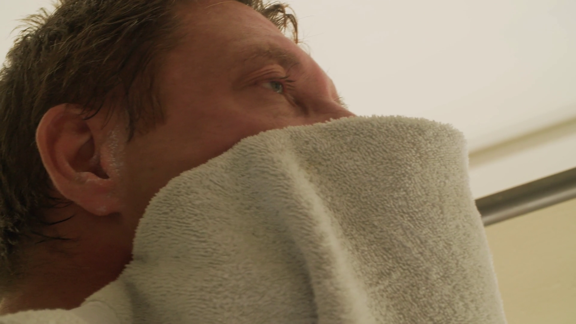 Very tired man uses bathroom towel to dampen & dry off face in morning