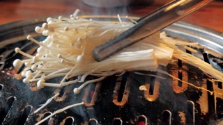 The cook prepares mushrooms on Korean BBQ gril plate. Tasty grilled food. . Mushroom barbecue roasted on metal grill. Diet vegan bbq.