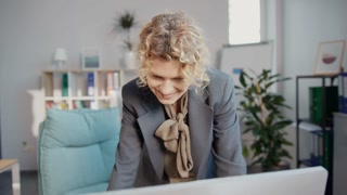 Horizontal shot of good-looking smiling Caucasian woman standing near desk and looking at laptop in office. Manager in modern office. New