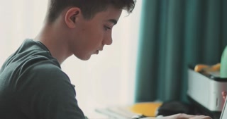 A serious teenager is sitting using laptop home room. frame side close-up keyboard touches hair attentive serious homework disappointed