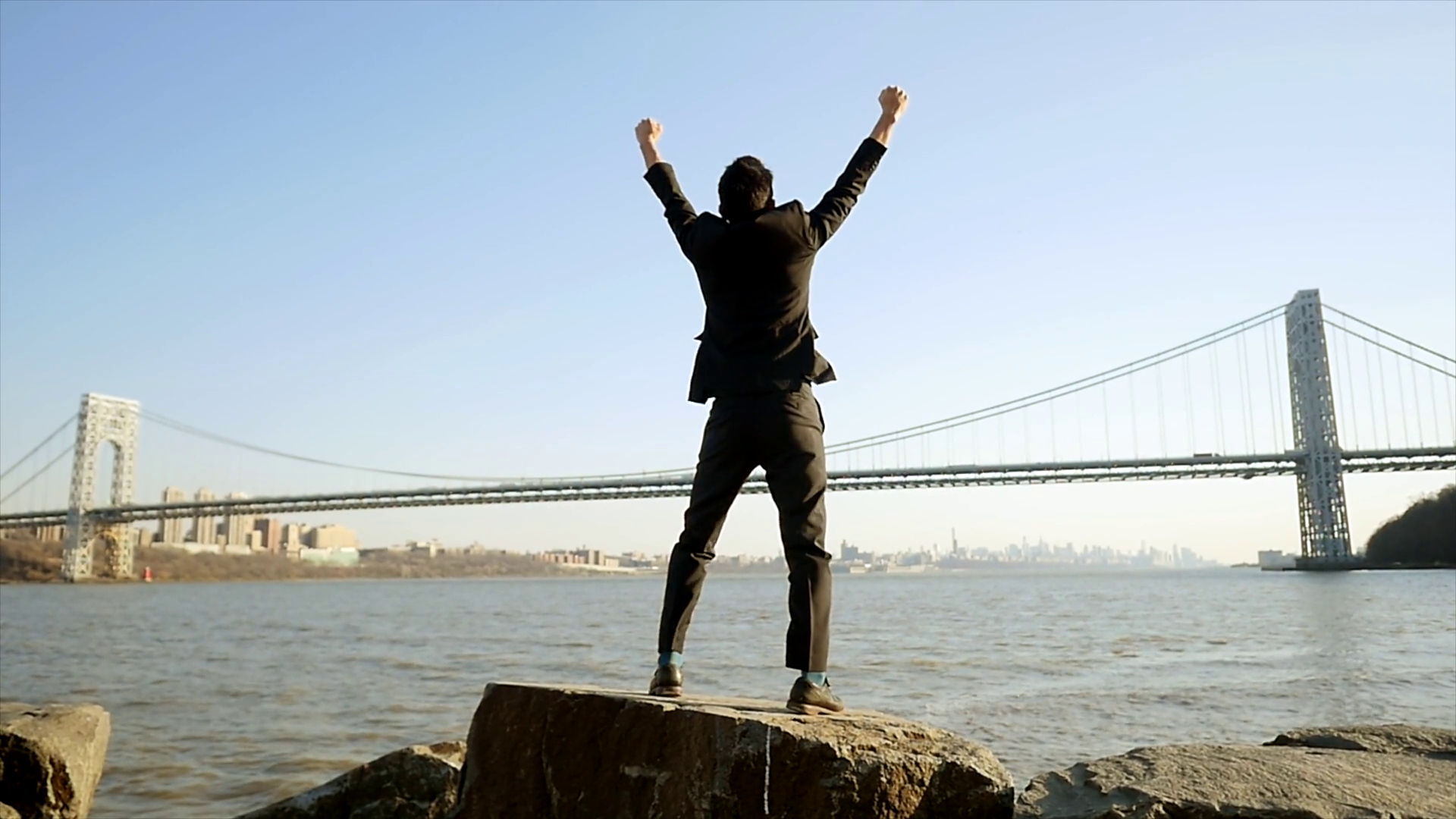successful man standing on top raising arms for wining victory pose