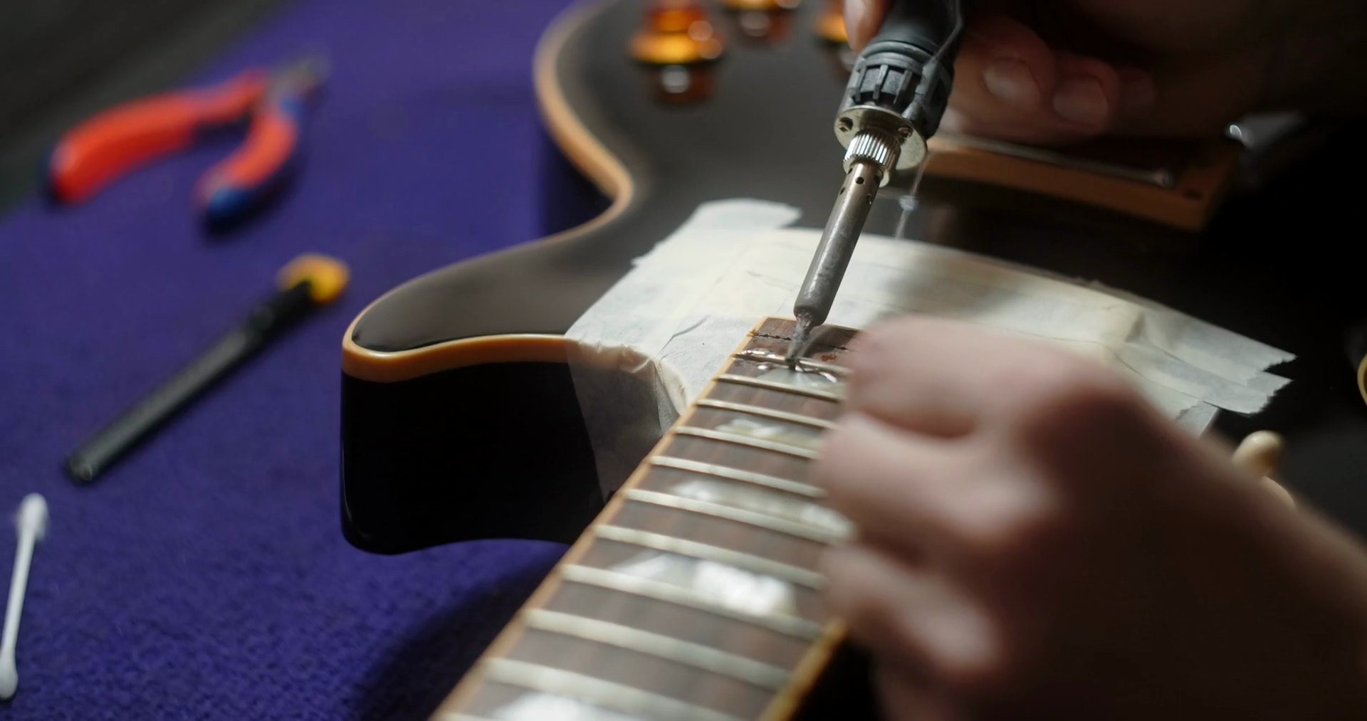 Luthier heats frets on guitar by soldering iron before refretting