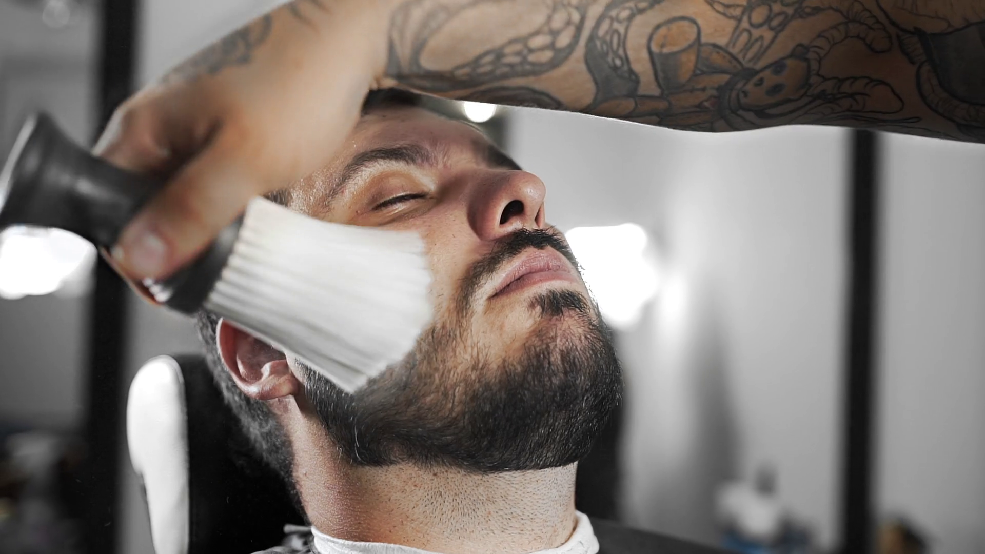 Barber whisks away sheared hairs from customer's shoulders by brush