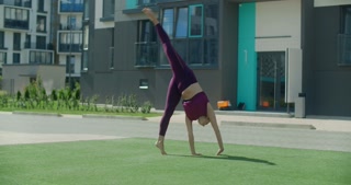 Athletic woman performs cartwheel in apartment building yard, city gymnastics, outdoor training, slow motion workout (4k 120p)