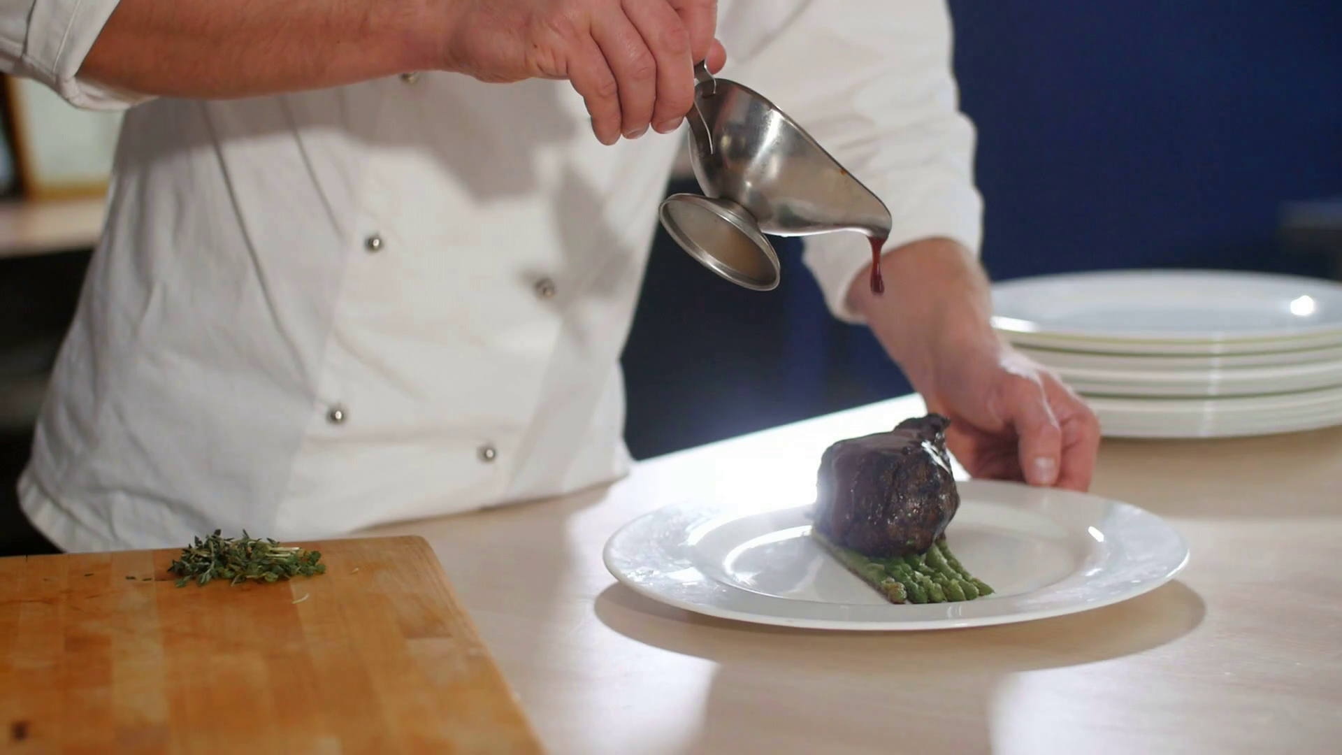 Chef plating up food in a restaurant pouring a gravy or sauce over the