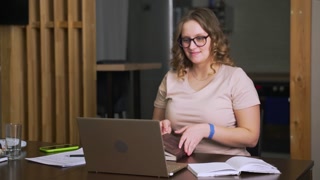 Woman with glasses is sitting at desk and studying at home, communicating with colleagues and friends via video over Internet on laptop. E-learning, video communication, quarantine, distance learning