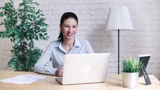 Smiling hipster girl talking and waving and Hello during a video call with a laptop sitting at the table at work. Cheerful business woman having a conference on the Internet via laptop.