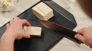 Chef cut cheese for Fried tofu with sesame seeds and spices on cast iron pan, cooking japanese salad. Healthy ingredient for cooking vegan