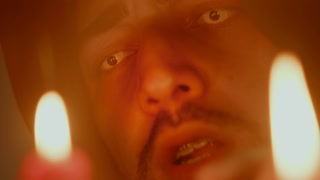 Evil sorcerer conjuring with burning candles, reading spell. Wicked magician making ritual in darkness, wizard with scary eyes using witchcraft, black magic. Halloween concept.