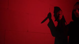 Creepy death silhouette walking with knife on red background. Mystical scary murderer going to kill. Halloween costume of killer. Horror scene movie of psycho serial.