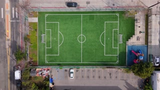 Aerial ascending shot over urban soccer green field with playground, parking lot, and street