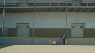 A businessman carrying a cargo pallet of goods in the background of a warehouse