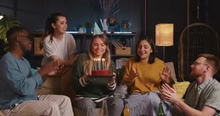 Birthday Celebration: Joyful woman blows on cake, dances with diverse friends at confetti house party