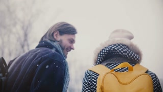 Happy couple holding hands, walking in snow with yellow backpacks