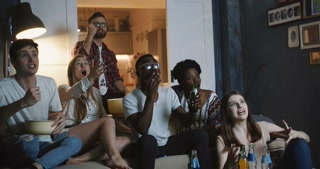 Close-up enthusiastic sports fans watch game at home, experience emotions, support each other with drinks (slow motion)