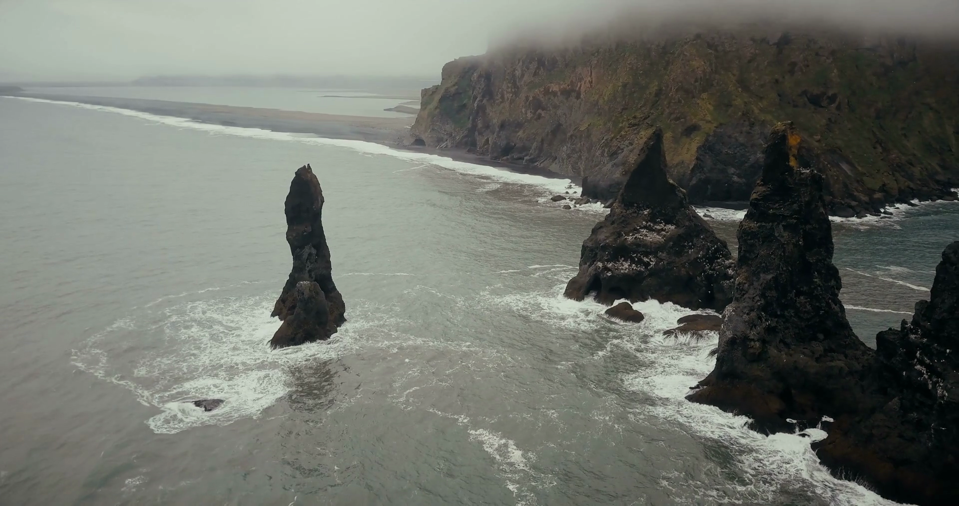 Copter flies away from the black volcanic beach and troll toes cliffs