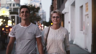 Happy smiling romantic couple hold hands and talk while walking along evening Soho, New York, enjoying evening city.