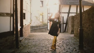 Portrait of adorable girl blowing kisses. Happy child posing on a sunny street. Sunlight flare. 4K.