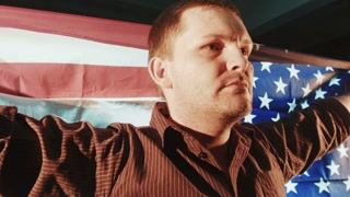 American patriotic male with American flag in hands on the back looking straight in the camera. Patriotic concept. Movement shot