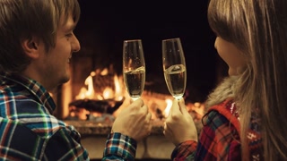 Couple toasting with champangne and kissing by the fireplace. Romantic cozy night by the fireplace. Back view. 4k graded from RAW, UHD, Ultra HD resolution.